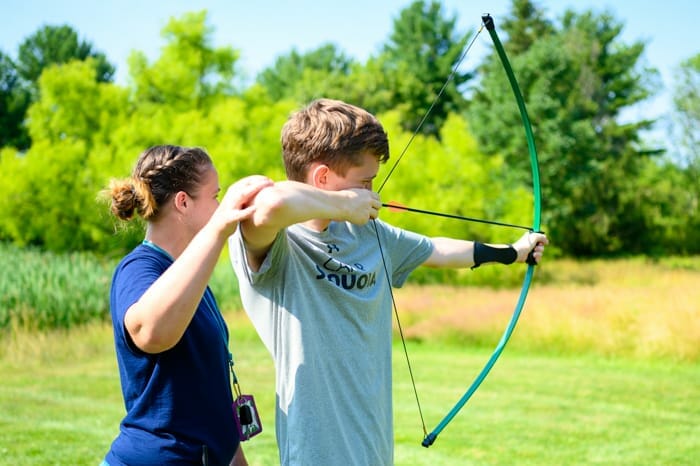 Archery instructor helping camper