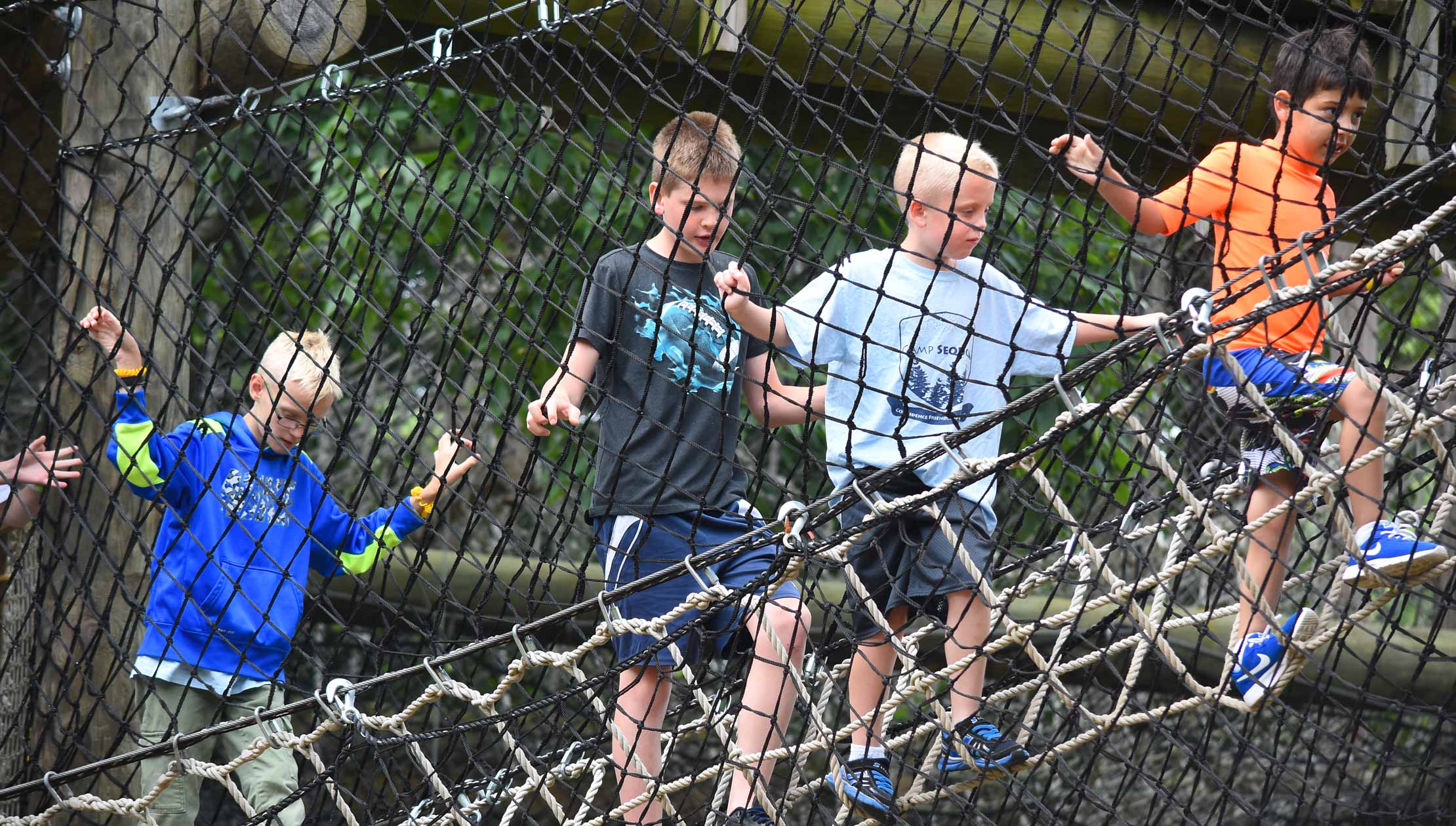 4 boys crossing a netted bridge
